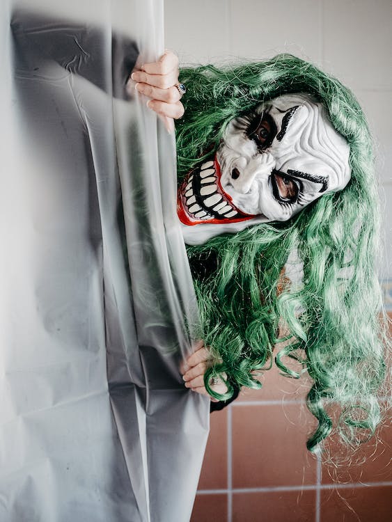 Potworny człowiek w zielonych włosach przypominający Jokera wyłania się zza zasłony od prysznica